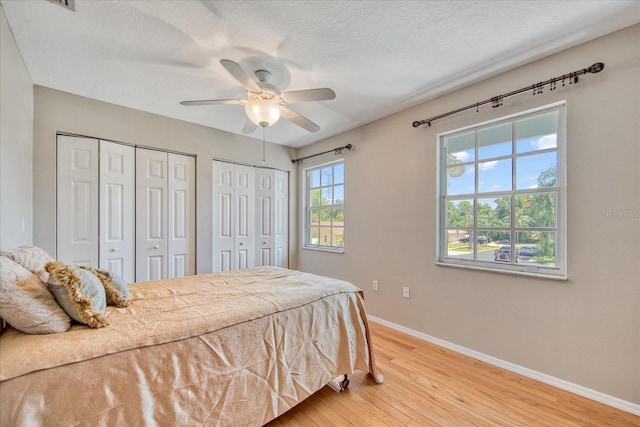 bedroom featuring wood-type flooring, a textured ceiling, ceiling fan, and multiple closets