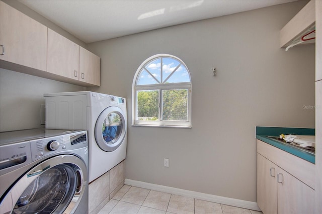 clothes washing area with cabinets, light tile patterned floors, and washer and dryer