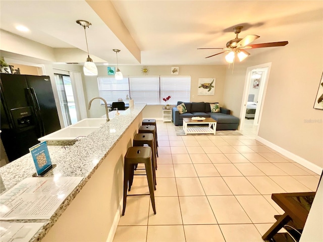 kitchen featuring light stone counters, black fridge with ice dispenser, ceiling fan, light tile patterned floors, and hanging light fixtures