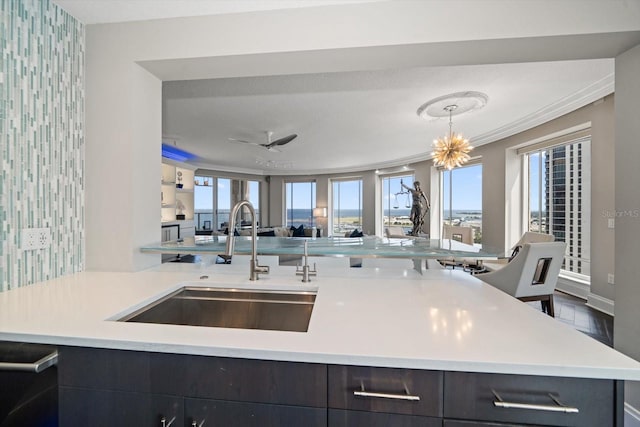 kitchen featuring sink, hanging light fixtures, kitchen peninsula, ceiling fan with notable chandelier, and ornamental molding