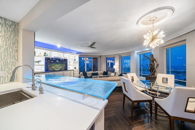 kitchen with sink, dark parquet floors, crown molding, decorative light fixtures, and ceiling fan with notable chandelier