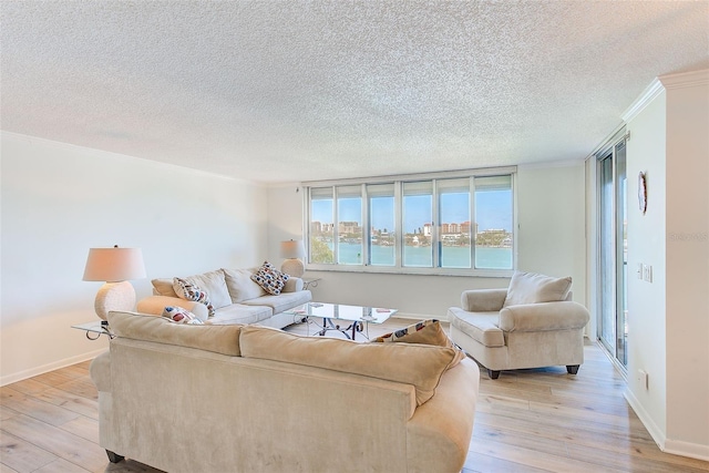 living room with a textured ceiling, a water view, ornamental molding, and light wood-type flooring