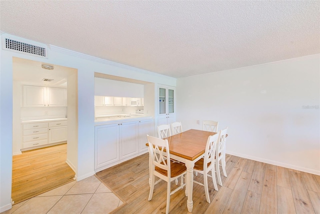 dining space with a textured ceiling, light hardwood / wood-style floors, and ornamental molding