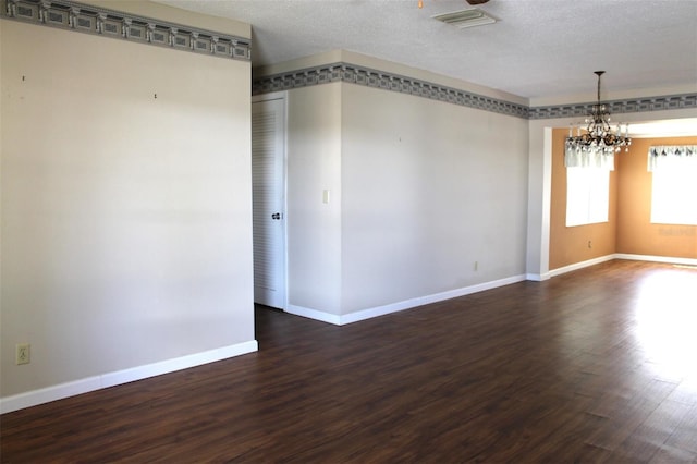 empty room featuring a notable chandelier, a textured ceiling, and dark wood-type flooring