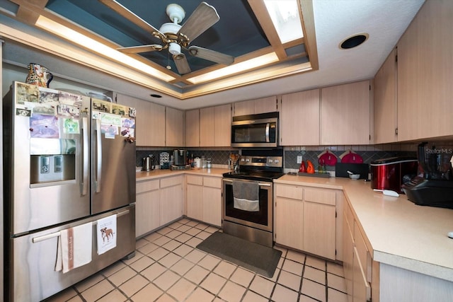 kitchen with light brown cabinets, ceiling fan, a tray ceiling, tasteful backsplash, and stainless steel appliances