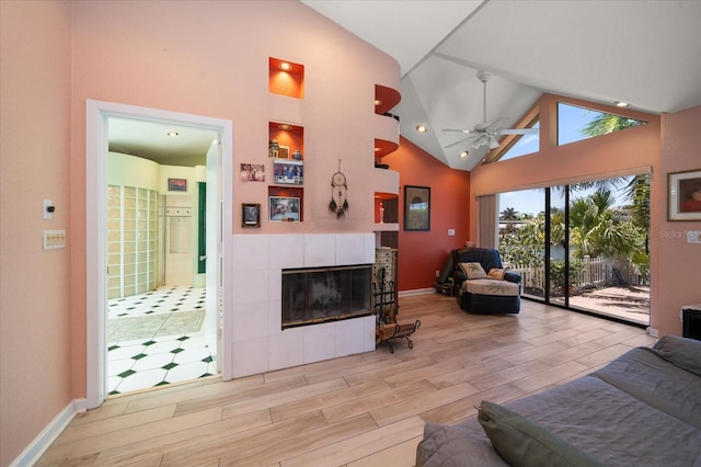 living room with a tile fireplace, ceiling fan, high vaulted ceiling, and light hardwood / wood-style floors