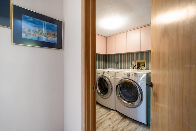 laundry area with washing machine and clothes dryer, cabinets, light hardwood / wood-style floors, and a textured ceiling