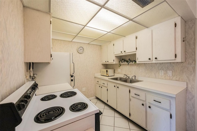 kitchen with a drop ceiling, white appliances, white cabinets, sink, and light tile patterned floors