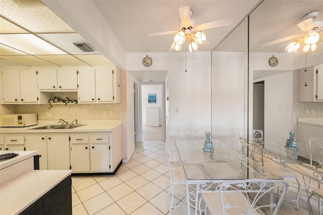 kitchen with white cabinets, sink, ceiling fan, light tile patterned floors, and a textured ceiling