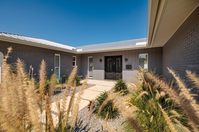 view of exterior entry with french doors, brick siding, and metal roof