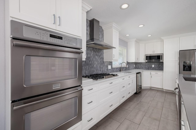 kitchen featuring a sink, white cabinets, appliances with stainless steel finishes, decorative backsplash, and wall chimney exhaust hood