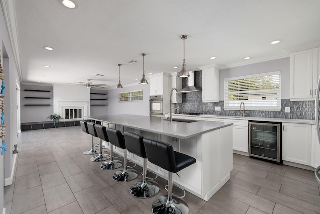 kitchen featuring wine cooler, a sink, open floor plan, a brick fireplace, and wall chimney exhaust hood