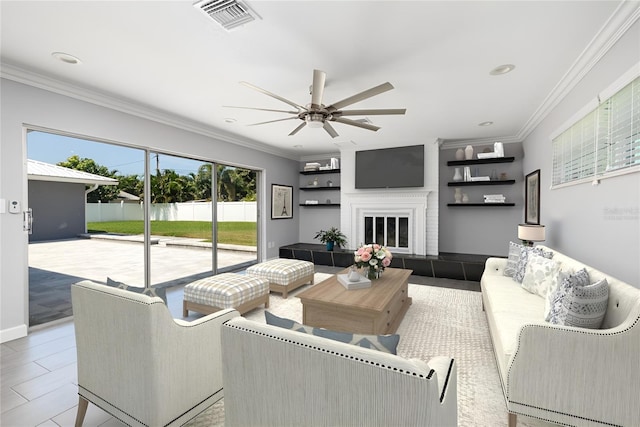 living room featuring crown molding, visible vents, a ceiling fan, a tile fireplace, and baseboards