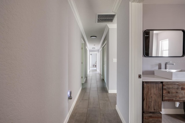 hallway featuring baseboards, a sink, visible vents, and crown molding