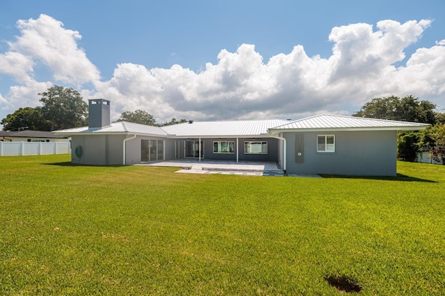 rear view of house featuring a patio, a chimney, metal roof, fence, and a yard