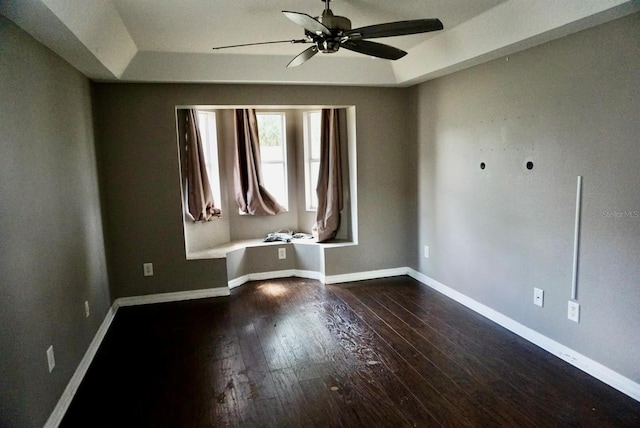 unfurnished room with ceiling fan, dark wood-type flooring, and a tray ceiling