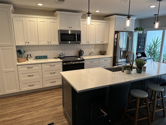 kitchen with appliances with stainless steel finishes, hanging light fixtures, and an island with sink