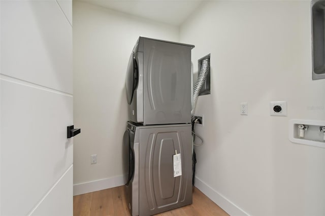 clothes washing area with light hardwood / wood-style flooring and stacked washer / drying machine