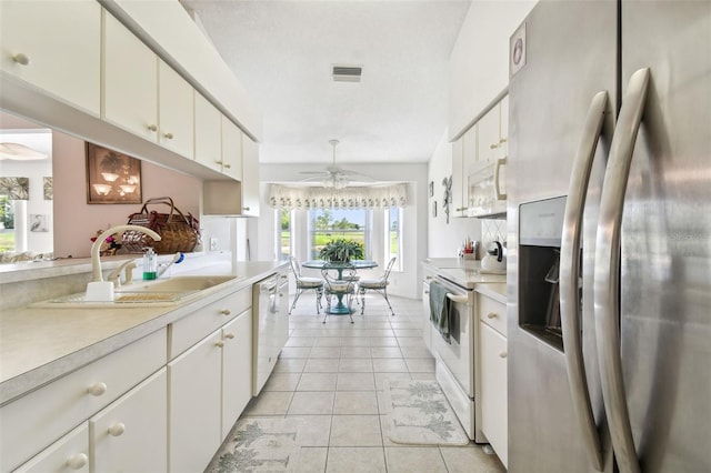 kitchen featuring white appliances, ceiling fan, sink, light tile patterned floors, and white cabinetry