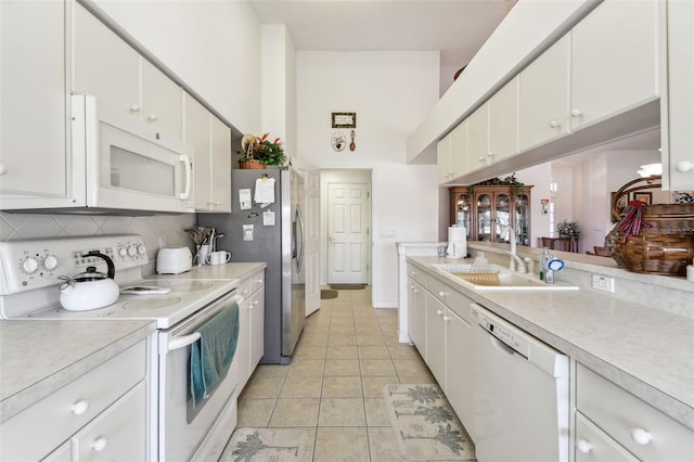 kitchen featuring white appliances, sink, decorative backsplash, light tile patterned floors, and white cabinetry