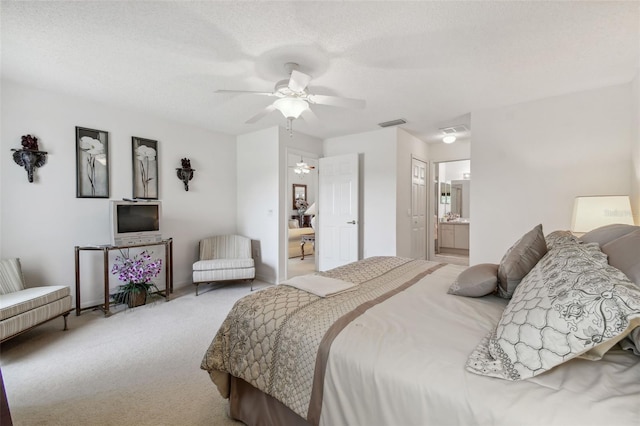 bedroom featuring a textured ceiling, ensuite bathroom, ceiling fan, and light colored carpet