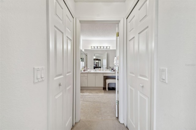 corridor with sink, light tile patterned floors, and a textured ceiling