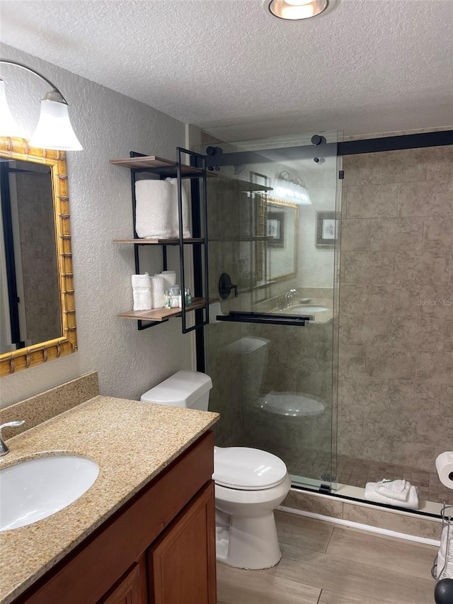 bathroom with a shower with door, vanity, a textured ceiling, and toilet