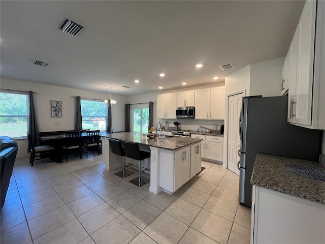 kitchen with a center island with sink, white cabinets, dark stone countertops, light tile patterned floors, and appliances with stainless steel finishes