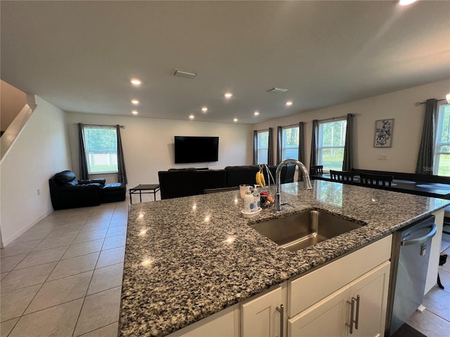 kitchen featuring sink, light tile patterned floors, dark stone countertops, dishwasher, and white cabinetry