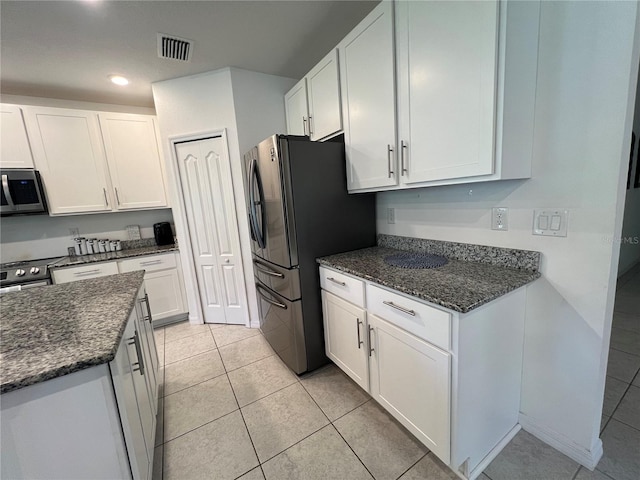 kitchen featuring dark stone countertops, white cabinets, stainless steel appliances, and light tile patterned floors