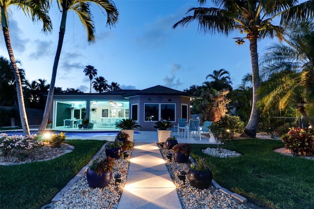 back house at dusk with a patio and a lawn