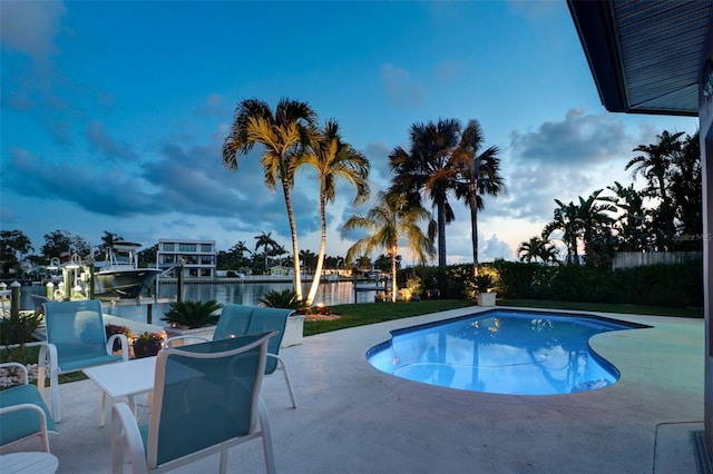 pool at dusk featuring a water view, a dock, and a patio