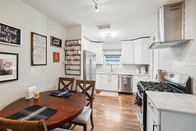 kitchen with sink, white cabinetry, stainless steel appliances, a textured ceiling, and wall chimney exhaust hood