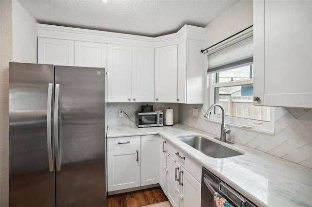 kitchen featuring appliances with stainless steel finishes, white cabinetry, sink, decorative backsplash, and light stone countertops