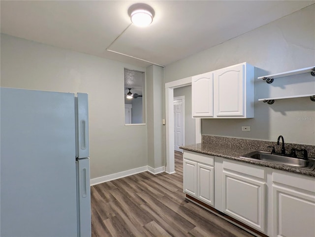 kitchen with white cabinetry, dark countertops, freestanding refrigerator, and a sink