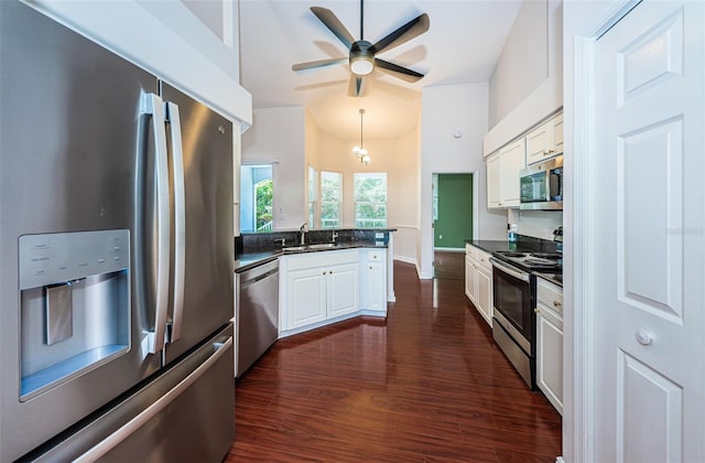 kitchen featuring stainless steel appliances, dark countertops, white cabinetry, a sink, and a peninsula