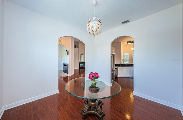 dining room featuring baseboards, arched walkways, dark wood finished floors, a textured ceiling, and a notable chandelier