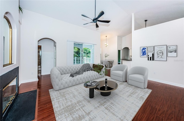 living area featuring a fireplace with flush hearth, arched walkways, a ceiling fan, and wood finished floors