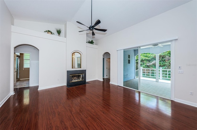 unfurnished living room featuring arched walkways, ceiling fan, wood finished floors, and a fireplace with flush hearth