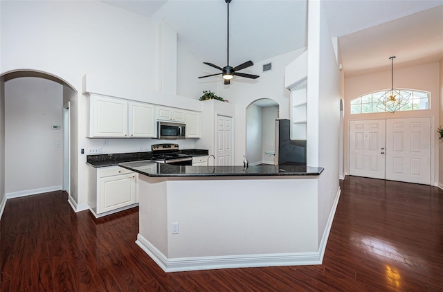 kitchen with arched walkways, stainless steel appliances, a peninsula, white cabinetry, and dark wood finished floors