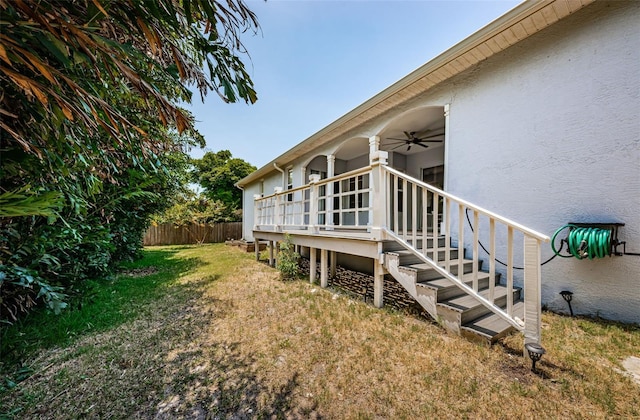 view of side of property with ceiling fan, a lawn, fence, and stucco siding