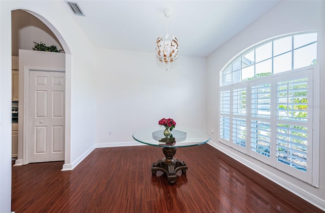 unfurnished dining area featuring baseboards, visible vents, arched walkways, wood finished floors, and an inviting chandelier