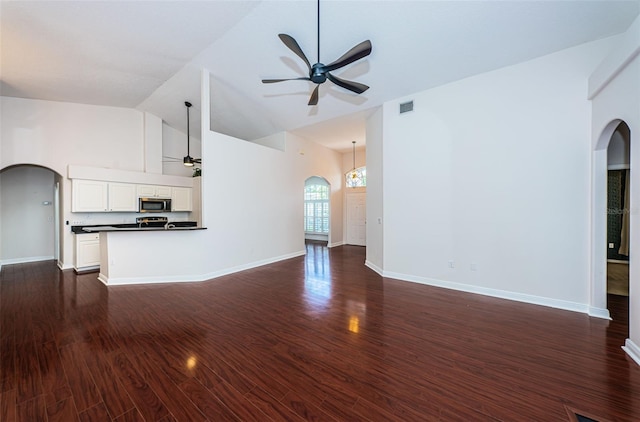 unfurnished living room featuring arched walkways, visible vents, dark wood-style floors, and a ceiling fan