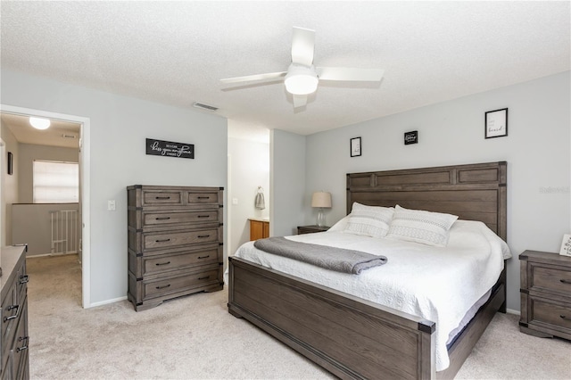 bedroom featuring ensuite bath, ceiling fan, light carpet, and a textured ceiling