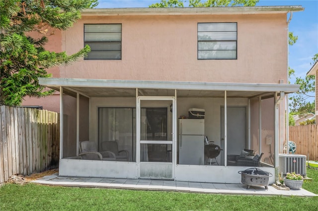 back of house featuring a lawn, an outdoor fire pit, cooling unit, and a sunroom