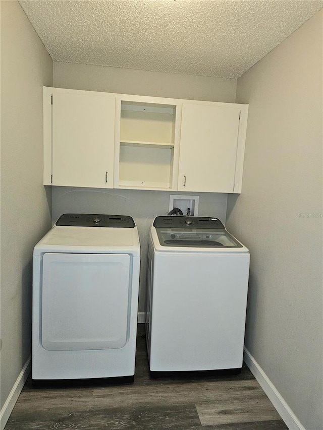 clothes washing area with dark hardwood / wood-style floors, washer and clothes dryer, cabinets, and a textured ceiling