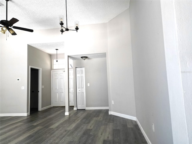 unfurnished room featuring ceiling fan with notable chandelier, a textured ceiling, a towering ceiling, and dark hardwood / wood-style floors