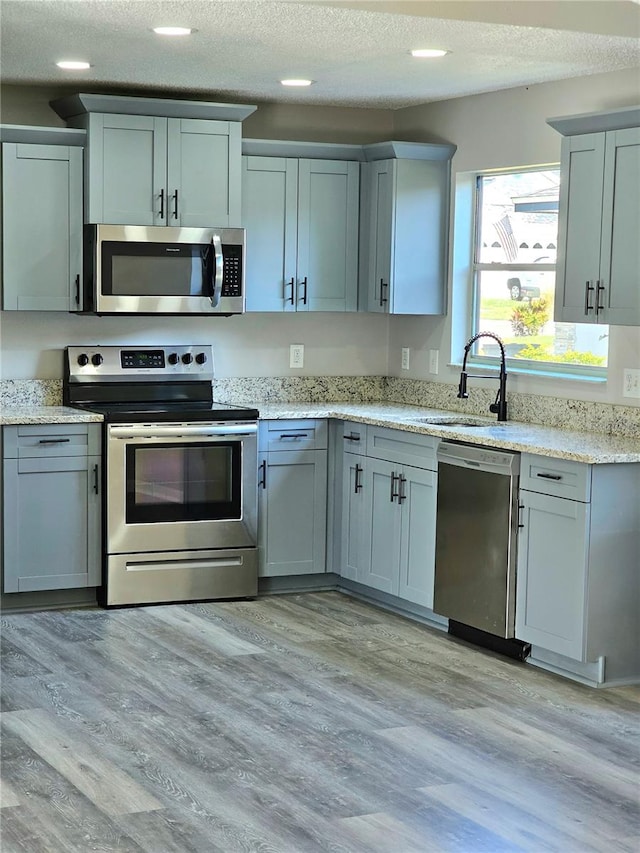 kitchen with light stone counters, a textured ceiling, stainless steel appliances, sink, and light hardwood / wood-style flooring