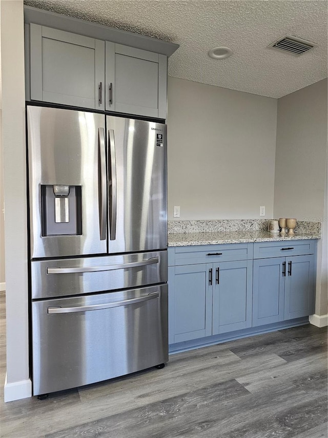 kitchen featuring stainless steel fridge, a textured ceiling, light hardwood / wood-style flooring, and light stone counters