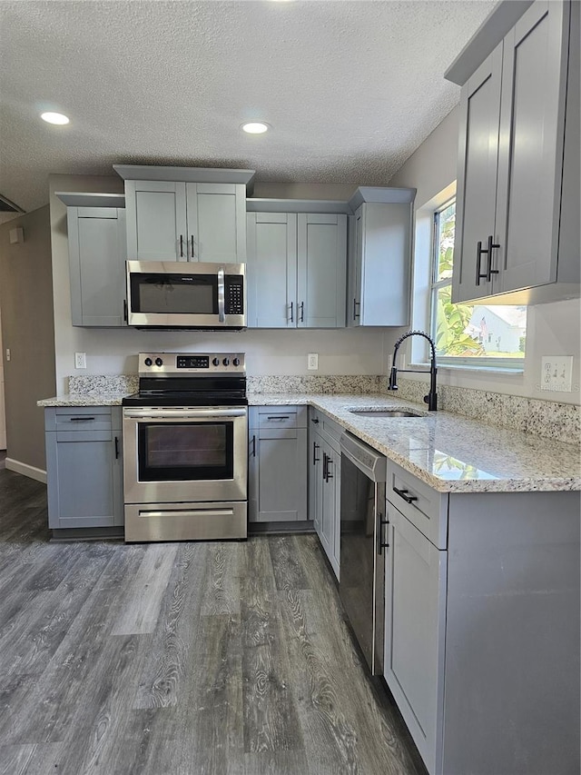 kitchen featuring sink, stainless steel appliances, light stone counters, a textured ceiling, and gray cabinets